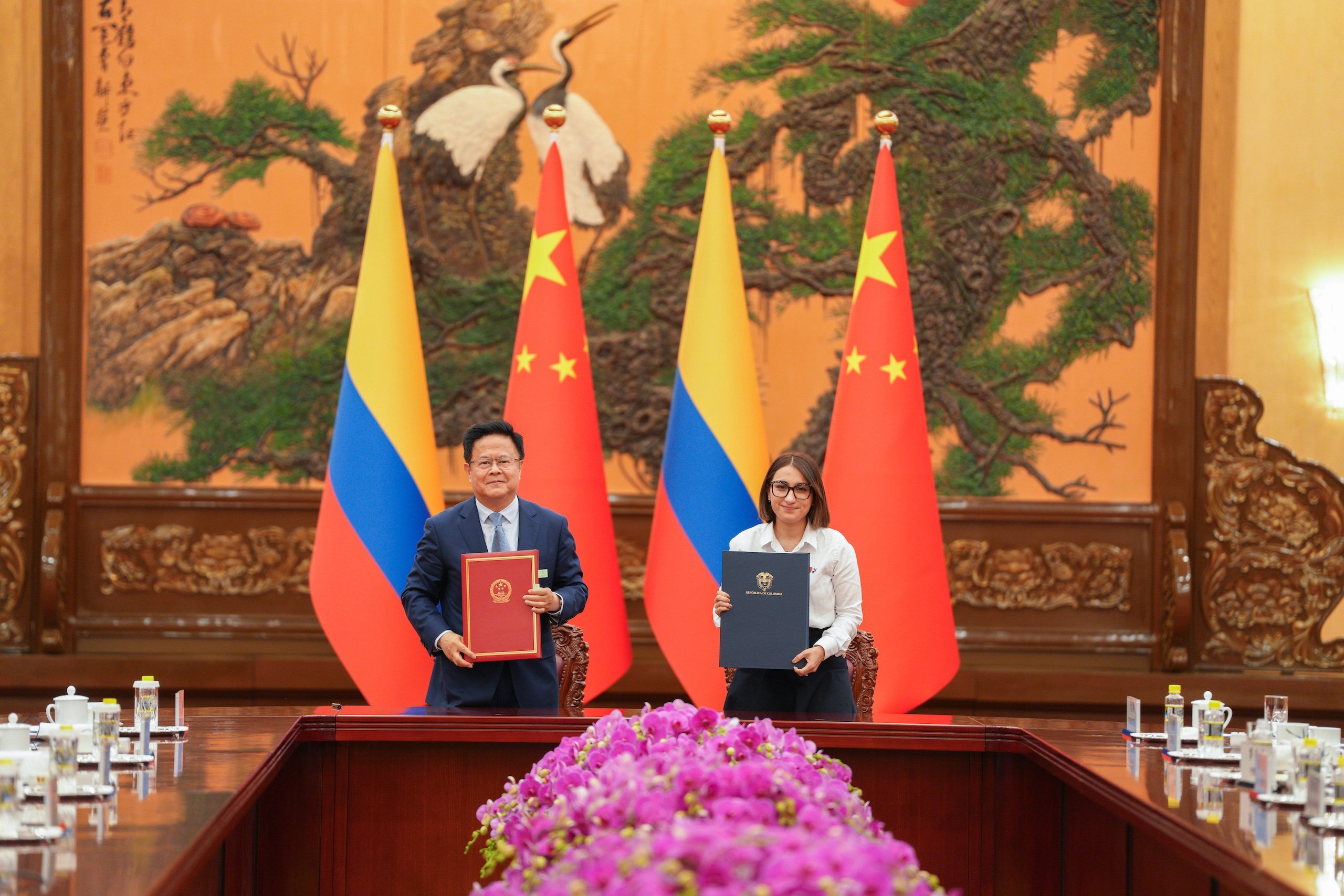 Two individuals standing beside a table, holding documents in their hands